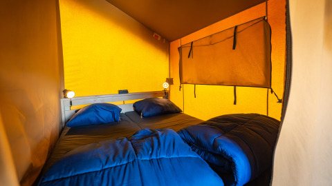 Gezellige slaapkamer met tweepersoonsbed en blauw beddengoed in de Compact safaritent op Camping de Molenhoek.