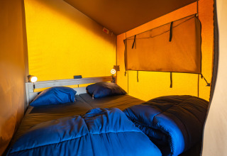 Gezellige slaapkamer met tweepersoonsbed en blauw beddengoed in de Compact safaritent op Camping de Molenhoek.