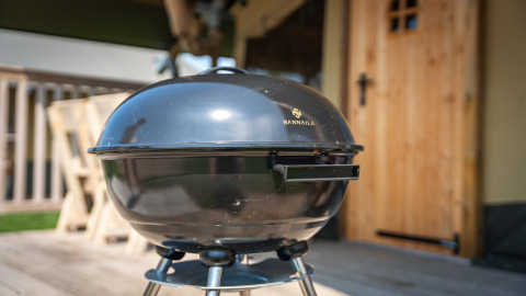 Zwarte barbecue bij safari tent ‘Compact’ op Camping de Molenhoek in Nederland op een houten terras.