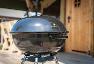 Zwarte barbecue bij safari tent ‘Compact’ op Camping de Molenhoek in Nederland op een houten terras.