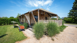 Safaritent genaamd Villatent Cottage met houten terras, omgeven door groen en onder blauwe lucht.