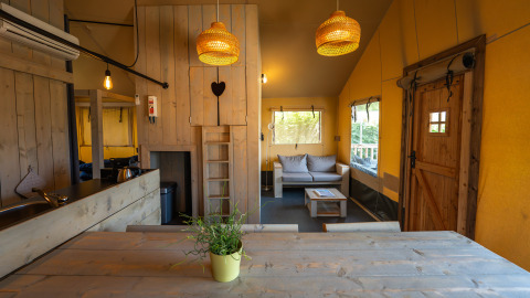 Vista interna di una tenda safari Villatent Cottage al Camping de Molenhoek con arredi in legno e divano.