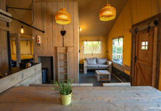 Vista interna di una tenda safari Villatent Cottage al Camping de Molenhoek con arredi in legno e divano.