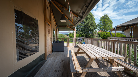 Terrazza in legno con tavolo da picnic presso la tenda safari Villatent Cottage al Camping de Molenhoek, Paesi Bassi.