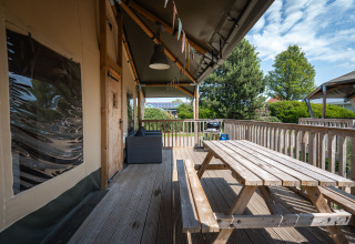 Terrazza in legno con tavolo da picnic presso la tenda safari Villatent Cottage al Camping de Molenhoek, Paesi Bassi.
