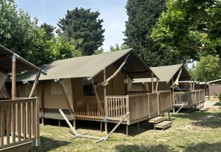 Tende safari con terrazze in legno al Villatent Outback, immerse in un campeggio verdeggiante e soleggiato.