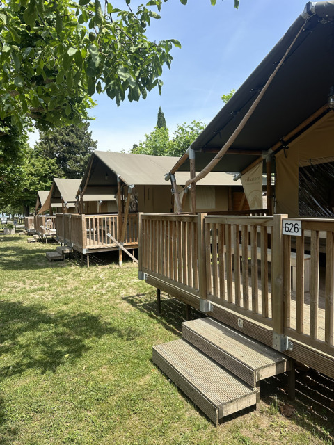 Safari tents with wooden porches at Camping Gasparina, Italy, shown during the day among green trees.