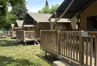 Tende safari con veranda in legno al Camping Gasparina in Italia, fotografate di giorno tra alberi verdi.