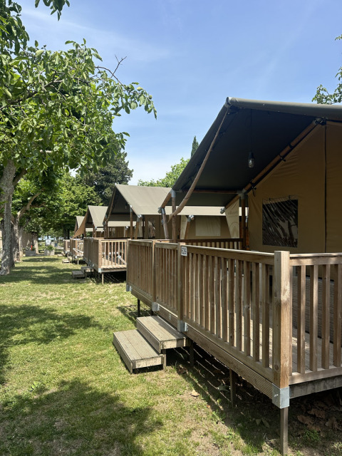 Safari-Zelte mit Holzbalkonen im Camping Gasparina, Italien, im Freien unter schattigen Bäumen.