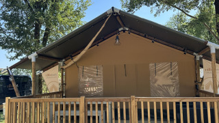 Foto di una tenda safari chiamata Outback con veranda in legno e gradini, circondata da alberi.