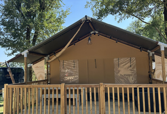 Ein Foto von einem Safari-Zelt namens Outback mit Holzveranda und Treppe, umgeben von Bäumen.