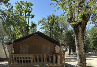 Safari-Zelt 'Outback' auf dem Camping Spina Family Collection in Italien, umgeben von Bäumen und Sonnenschein.