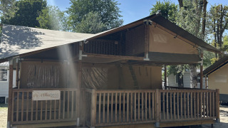 Tenda safari chiamata Ranger con veranda in legno, circondata da alberi sotto un cielo limpido.