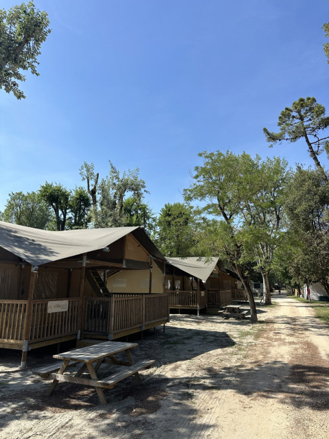 Tende safari al Camping Spina Family Collection in Italia con tavoli da picnic e cielo sereno.