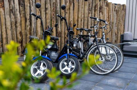 Bicycles and electric scooters parked on a lodge patio, with a wooden fence and plants in the foreground.