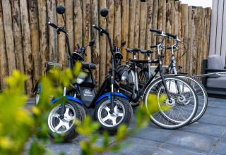 Bicycles and electric scooters parked on a lodge patio, with a wooden fence and plants in the foreground.