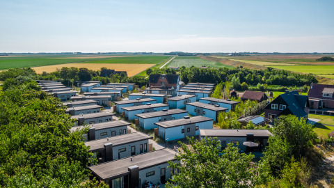 Aerial view of modern lodges surrounded by green fields and trees, set in a rural landscape on a sunny day.
