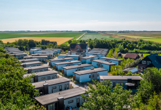Aerial view of modern lodges surrounded by green fields and trees, set in a rural landscape on a sunny day.