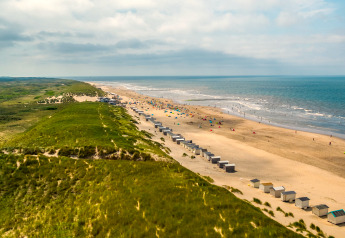 Grande spiaggia sabbiosa con dune erbose e cabine vicino a un lodge, onde del mare e cielo sullo sfondo.