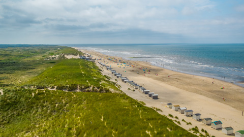 A wide sandy beach with grassy dunes and beach cabins near a lodge, ocean waves and sky in the distance.