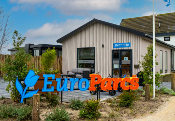 Edificio de recepción de EuroParcs con letrero azul Receptie y zona ajardinada en el exterior.