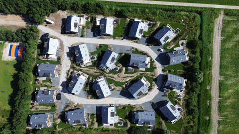Aerial view of a modern lodge with vacation homes surrounded by greenery and fields, seen from above.