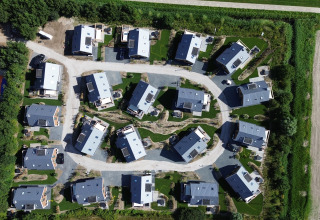 Aerial view of a modern lodge with vacation homes surrounded by greenery and fields, seen from above.