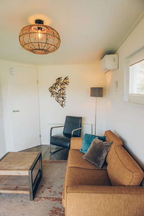 Gemütliches Wohnzimmer im Tiny House 'Valleichalet' im Ferienpark Ackersate, Niederlande, mit Sofa.