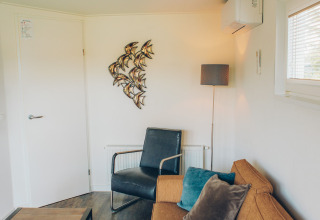 Living area of tiny house 'Valleichalet' at Holiday park Ackersate, Netherlands, with sofa and decor.