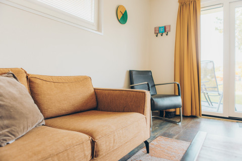 Modern living room in a tiny house at Valleichalet, Holiday park Ackersate, Netherlands, with sofa and chair.