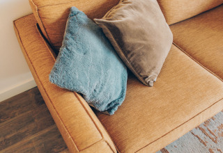 Acogedor interior de tiny house Valleichalet con sofá mostaza y cojines en Holiday park Ackersate, Países Bajos.