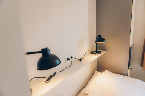 Moderne zwarte bureaulampen op plank bij bed in tiny house Valleichalet in vakantiepark Ackersate, Nederland.