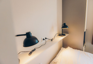 Moderne zwarte bureaulampen op plank bij bed in tiny house Valleichalet in vakantiepark Ackersate, Nederland.