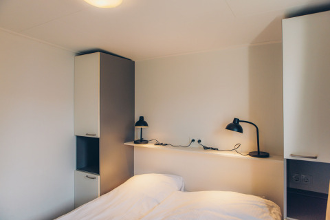 Slaapkamer in tiny house 'Valleichalet' op Holiday park Ackersate in Nederland met bed en lampen.