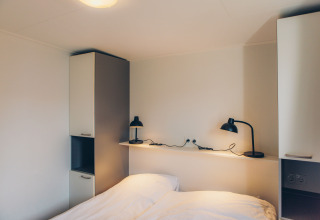 Soveværelse i tiny house 'Valleichalet' med dobbeltseng og læselamper på Holiday park Ackersate.