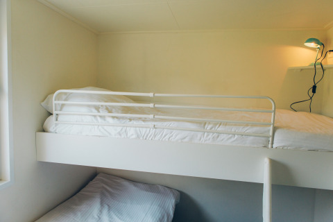 Minimalist bunk bed in a tiny house at Valleichalet, Holiday park Ackersate, Netherlands, with lamp on wall.