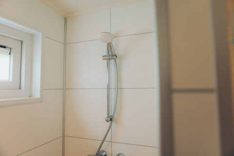 Shower with white tiled wall and small window in the Valleichalet tiny house at Holiday park Ackersate.