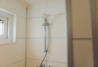 Shower with white tiled wall and small window in the Valleichalet tiny house at Holiday park Ackersate.