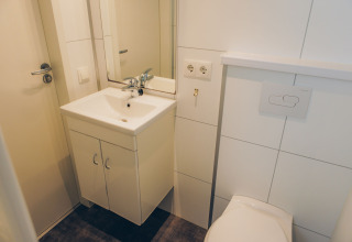 Small bathroom with white sink, mirror, toilet, and sockets at Valleichalet, Ackersate, Netherlands.