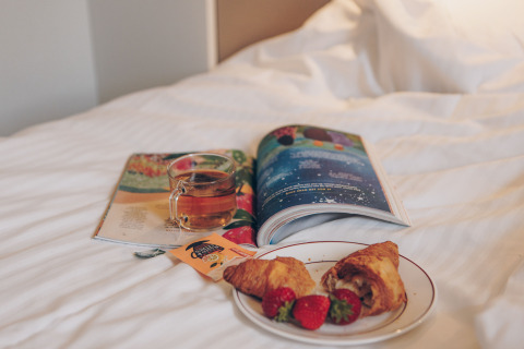 A cup of tea, croissants with strawberries, and a magazine on a bed in a tiny house at Valleichalet, Netherlands.