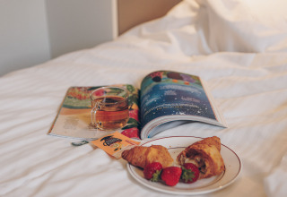 Een kopje thee, croissants met aardbeien en een tijdschrift op bed in een tiny house in Valleichalet, Nederland.
