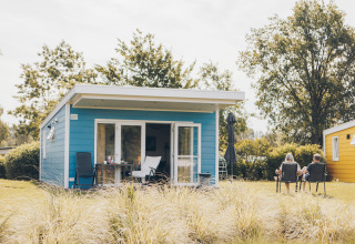 Two people relaxing outside the blue Valleichalet tiny house at Holiday park Ackersate in the Netherlands.