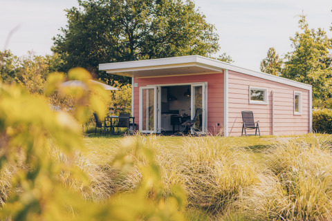 Valleichalet tiny house at Holiday park Ackersate, Netherlands, with grassy lawn, patio chairs, and table.