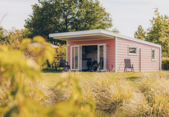 Valleichalet tiny house at Holiday park Ackersate, Netherlands, with grassy lawn, patio chairs, and table.