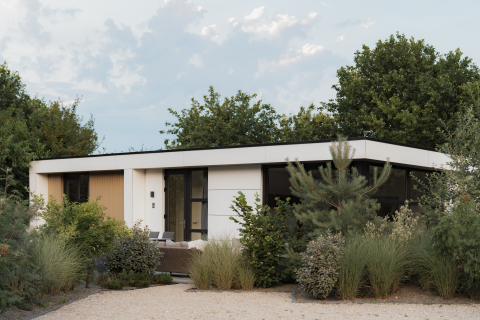 Moderne lodge Villa Bloomingdale, omringd door groen en bomen, onder een deels bewolkte blauwe lucht.