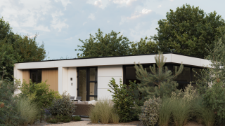 Moderne lodge Villa Bloomingdale, omringd door groen en bomen, onder een deels bewolkte blauwe lucht.
