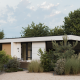 Moderne lodge Villa Bloomingdale, omringd door groen en bomen, onder een deels bewolkte blauwe lucht.