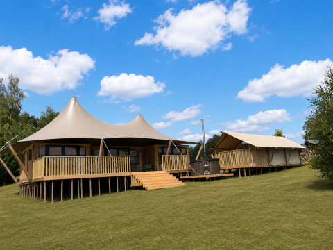 Safari tent Glamfield Lodge Deluxe met hot tub en houten terras in een ruim, groen landschap.