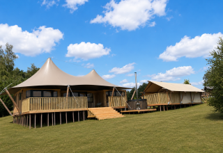 Safari tent Glamfield Lodge Deluxe met hot tub en houten terras in een ruim, groen landschap.