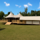 Safari tent Glamfield Lodge Deluxe met hot tub op een grasveld, omgeven door bomen en blauwe lucht.